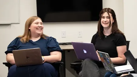 Two students with laptops talking and laughing.